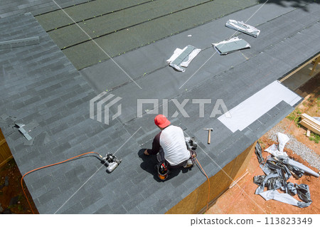 With assistance an air nail gun, professional roofing contractor installed new asphalt bitumen shingles on roof of house With assistance an air nail gun, professional roofing contractor installed new asphalt bitumen shingles on roof of house 113823349