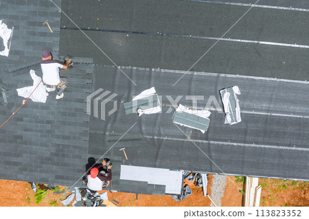 With help an air nail gun, professional roofing contractor installs new asphalt bitumen shingles on roof of house With help an air nail gun, professional roofing contractor installs new asphalt bitumen shingles on roof of house 113823352