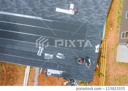 Roofer installing new asphalt bitumen shingles with air nail guns Roofer installing new asphalt bitumen shingles with air nail guns 113823355
