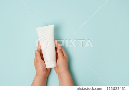 Child hands holding white cream tube on light blue background. Care about clean and soft body skin. Daily children beauty product 113823461