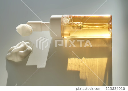 Beige facial foam with a dispenser and brush in the rays of the setting sun. 113824010