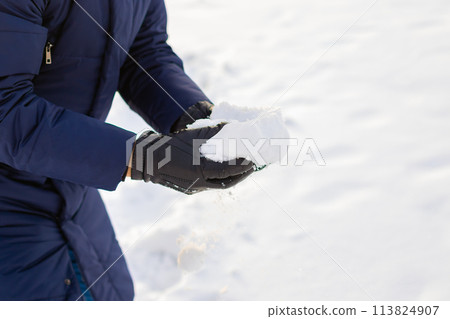 pile of snow in hands after heavy snowfall. man in gloves and winter clothes takes snow in his hands. leisure activities, snowball fight game 113824907