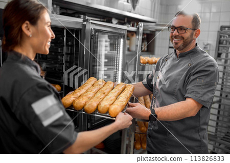 Colleagues working in a bakery and holding a tray with fresh buns 113826833