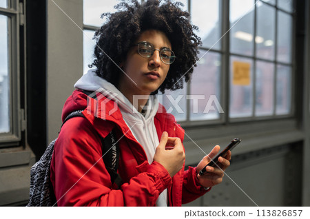 Curly-haired young guy in red jacket with a phone in hands Curly-haired young guy in red jacket with a phone in hands 113826857