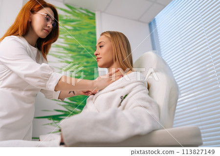 Low-angle view of professional female cardiologist attaching holter sensors on woman patient with heart disease. Young woman during functional rehabilitation in cardiology room in clinic. Low-angle view of professional female cardiologist attaching holter sensors on woman patient with heart disease. Young woman during functional rehabilitation in cardiology room in clinic. 113827149