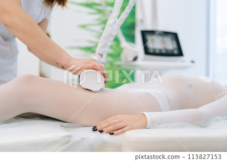 Cropped shot of unrecognizable young woman client getting beauty therapy against cellulite with LPG machine on leg for lifting body. Close-up hands of female therapist using lipomassage tool. 113827153
