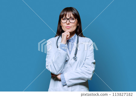 Confident serious female doctor looking at camera on blue background Confident serious female doctor looking at camera on blue background 113827182