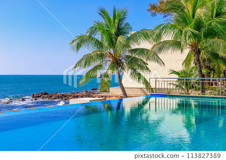 View of the outdoor pool by the sea. There is a lush palm tree next to the pool. Sanya, China. View of the outdoor pool by the sea. There is a lush palm tree next to the pool. Sanya, China. 113827389