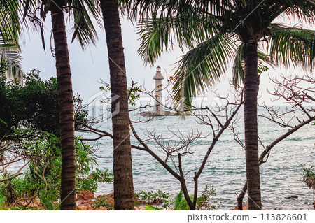 View of the lighthouse in the sea near the rocky shore through the palm trees. Sanya, China View of the lighthouse in the sea near the rocky shore through the palm trees. Sanya, China 113828601