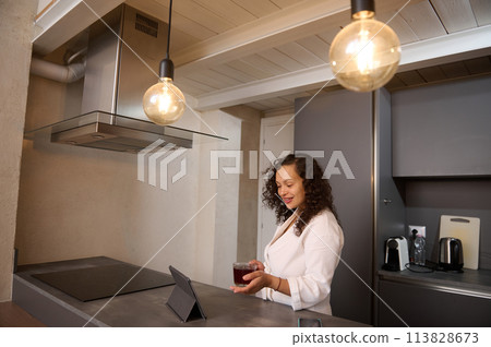 Happy millennial pretty woman in white bathrobe, relaxing at home, making a video call on digital tablet, standing at kitchen counter in modern home interior. Internet and mobile communication concept Happy millennial pretty woman in white bathrobe, relaxing at home, making a video call on digital tablet, standing at kitchen counter in modern home interior. Internet and mobile communication concept 113828673