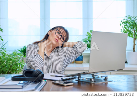 Tired middle-aged woman sitting at her workplace, desk with computer 113829738