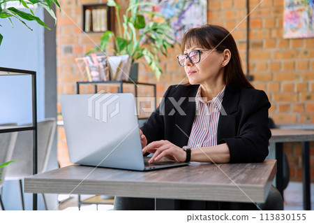 Middle-aged business woman working remotely with laptop in coworking Middle-aged business woman working remotely with laptop in coworking 113830155