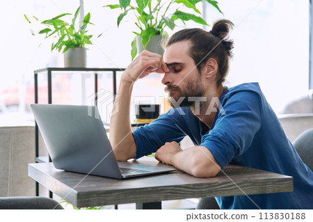 Young tired man working with laptop computer having headache fatigue Young tired man working with laptop computer having headache fatigue 113830188