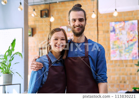 Hugging couple of colleagues partners young man and woman in aprons at workplace Hugging couple of colleagues partners young man and woman in aprons at workplace 113830221