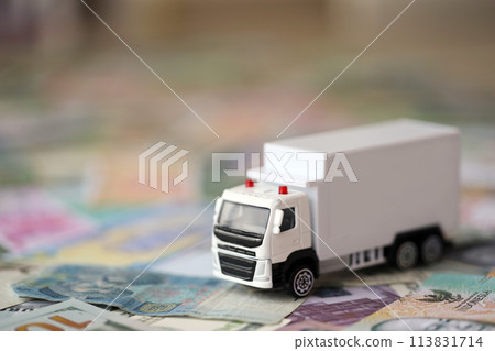 Delivery truck on many banknotes of different currency. Background of trucking or moving concept close up Delivery truck on many banknotes of different currency. Background of trucking or moving concept close up 113831714