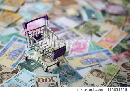 Supermarket trolley on many banknotes of different currency. Background of shopping worldwide close up Supermarket trolley on many banknotes of different currency. Background of shopping worldwide close up 113831716