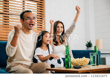 A family of fans gathers on the sofa to watch a football match on TV. Their cheers, encouragement, and togetherness reflect the joy of the game and the shared happiness in the room. 113831875