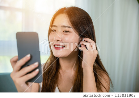 Happy relaxed female touching earbuds listen song on mobile phone in bright living room at home, Lifestyle Asian young woman wearing wireless earphones listening to favorite song on her smartphone Happy relaxed female touching earbuds listen song on mobile phone in bright living room at home, Lifestyle Asian young woman wearing wireless earphones listening to favorite song on her smartphone 113831902