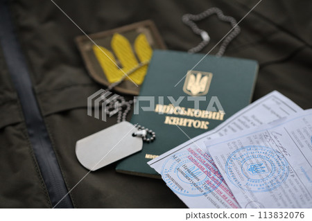Military token or army ID ticket with mobilization notice lies on green ukrainian military uniform indoors close up 113832076