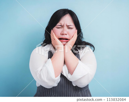 A chubby woman with her hands on her cheeks, looking displeased 113832084