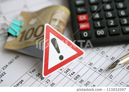 Attention sign and calculation results in schedules lies on table with canadian money bills, calculator and pen close up. Taxation and annual accountant paperwork in Canada Attention sign and calculation results in schedules lies on table with canadian money bills, calculator and pen close up. Taxation and annual accountant paperwork in Canada 113832097
