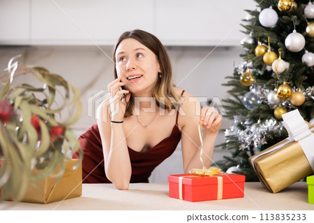 Attractive woman is preparing presents and discussing it with someone on a mobile phone Attractive woman is preparing presents and discussing it with someone on a mobile phone 113835233