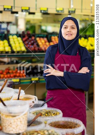 Young woman in hijab selling olives in supermarket Young woman in hijab selling olives in supermarket 113835308