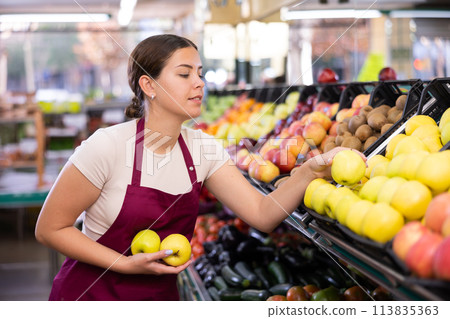 Female supermarket salesperson setting out apples on shelves Female supermarket salesperson setting out apples on shelves 113835363