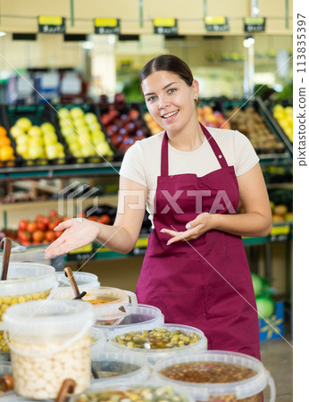 Young woman in uniform sells olives in supermarket Young woman in uniform sells olives in supermarket 113835397