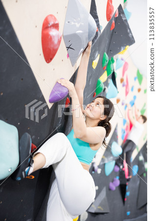 Young Asian woman climbs steep artificial wall in sports complex and trains endurance 113835557