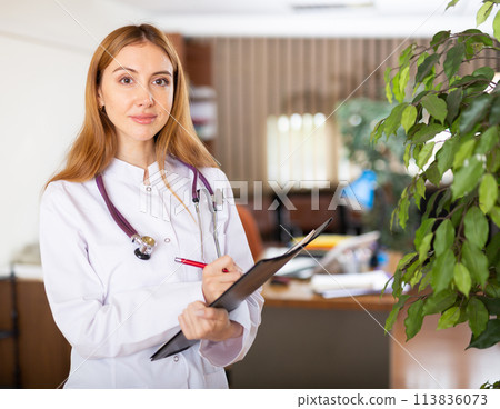 Young woman therapist writes notes on a tablet, standing in a office 113836073