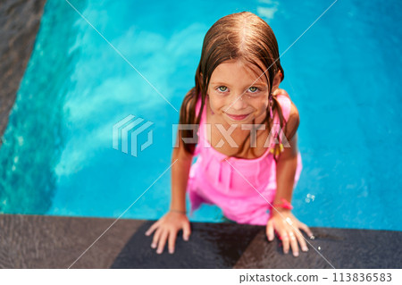 Happy girl in pink swimsuit enjoys summer day in kids pool at resort. Child smiles, plays in water, leisure activity. Outdoor family vacation, tropical climate, fun swimming, childhood joy. Happy girl in pink swimsuit enjoys summer day in kids pool at resort. Child smiles, plays in water, leisure activity. Outdoor family vacation, tropical climate, fun swimming, childhood joy. 113836583