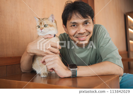 asian man smile and happy during play with his gold british cat in coffee shop asian man smile and happy during play with his gold british cat in coffee shop 113842029