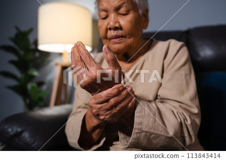 senior woman suffering from pain in wrist while sitting on sofa in living room at night senior woman suffering from pain in wrist while sitting on sofa in living room at night 113843414