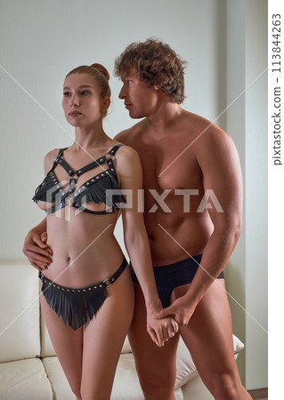 Young man and woman standing in BDSM costumes at home 113844263