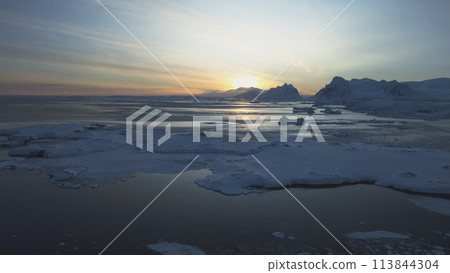 Dawn over Antarctic coast. Polar night sunset. Ocean covered ice. Top above aerial view. Antarctica snow mountain. Sky sunrise Antarctica winter. Open water. Beautiful sky landscape. Top Drone Flight 113844304