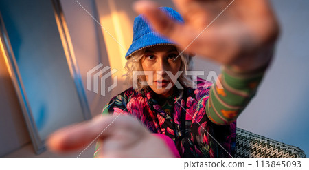 a woman wearing a blue hat and a colorful jacket is sitting on a couch 113845093