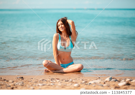 Summer vacation concept. A young pretty caucasian woman sitting crossed legs on the oceans beach 113845377