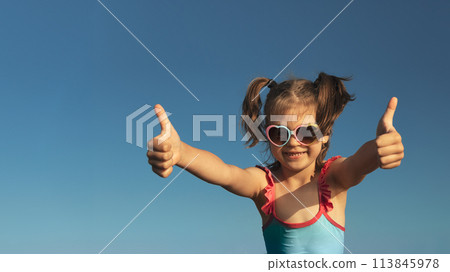 Portrait of laughing girl of 6 years in blue swimsuit and heart-shaped sunglasses gesturing super, fine against blue sky, banner Portrait of laughing girl of 6 years in blue swimsuit and heart-shaped sunglasses gesturing super, fine against blue sky, banner 113845978