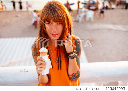 Top view portrait of young tanned beautiful Caucasian woman with tattoos holds ice cream and looking at camera. Concept of freedom and psychology 113846095