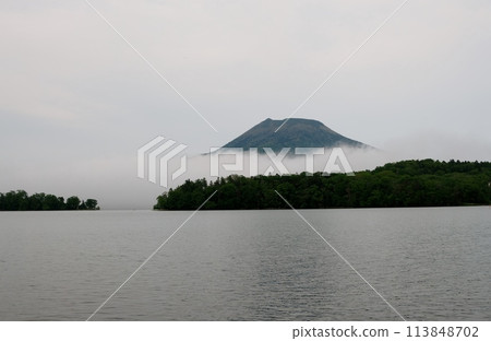 Mount Oakan seen through a clearing in the fog Mount Oakan seen through a clearing in the fog 113848702