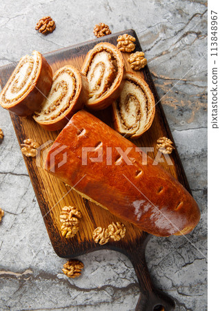 Sweet baked nut roll filled with walnuts and honey close-up on a wooden board on the table. Vertical top view 113848967