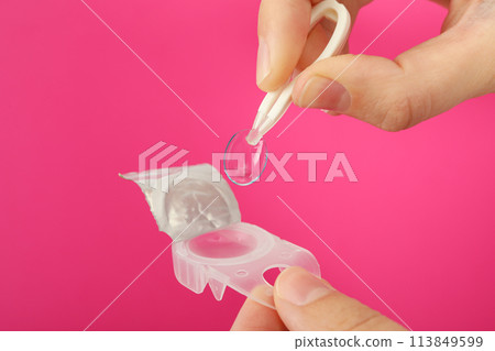 Plastic tweezers hold a clear eye lens close-up 113849599