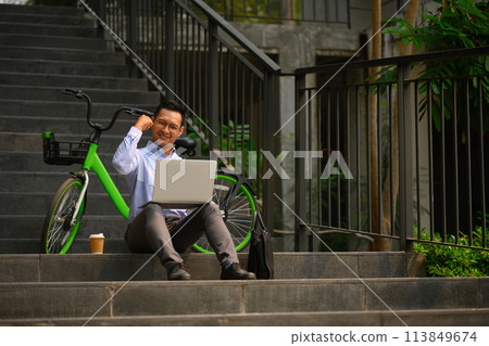 Happy adult businessman celebrating success, with raised hands in front of office building 113849674