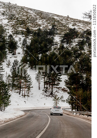 A vehicle navigates the snowy mountain road with caution 113850822