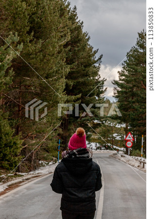 A person in a pink hat strolls on a snowy thoroughfare A person in a pink hat strolls on a snowy thoroughfare 113850833