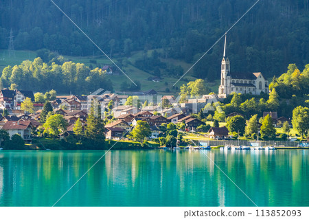 Swiss village Lungern with traditional houses, old church Alter Kirchturm along lovely emerald green lake Lungerersee, canton of Obwalden Switzerland Swiss village Lungern with traditional houses, old church Alter Kirchturm along lovely emerald green lake Lungerersee, canton of Obwalden Switzerland 113852093