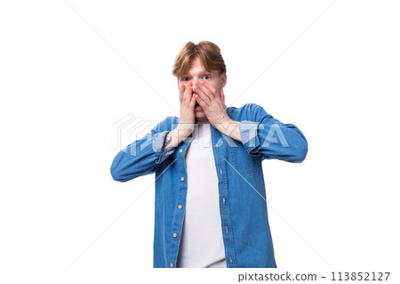 a young red-haired guy dressed in a blue shirt over a T-shirt looks at the camera in surprise a young red-haired guy dressed in a blue shirt over a T-shirt looks at the camera in surprise 113852127