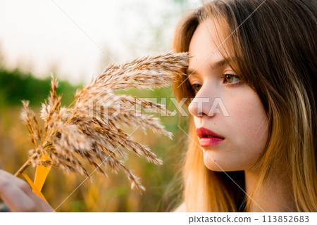 Beautiful young girl wearing blank gray t-shirt and black jeans posing against high green and yellow grass in early warm autumn. Outdoor portrait of beautiful female model. Close-up. 113852683