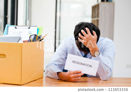 Man at desk with resignation letter, pondering his decision beside a packed box. Man at desk with resignation letter, pondering his decision beside a packed box. 113853338